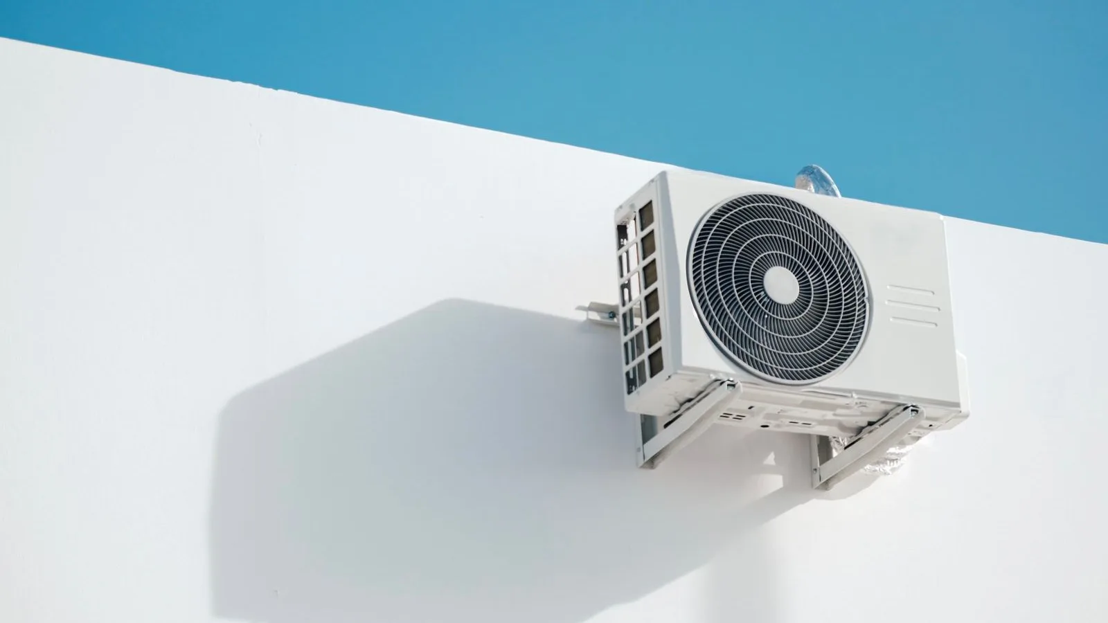 Best DIY mini split self-install with pre-charged line set: a ductless mini split outdoor condenser mounted on a white exterior wall under a clear blue sky
