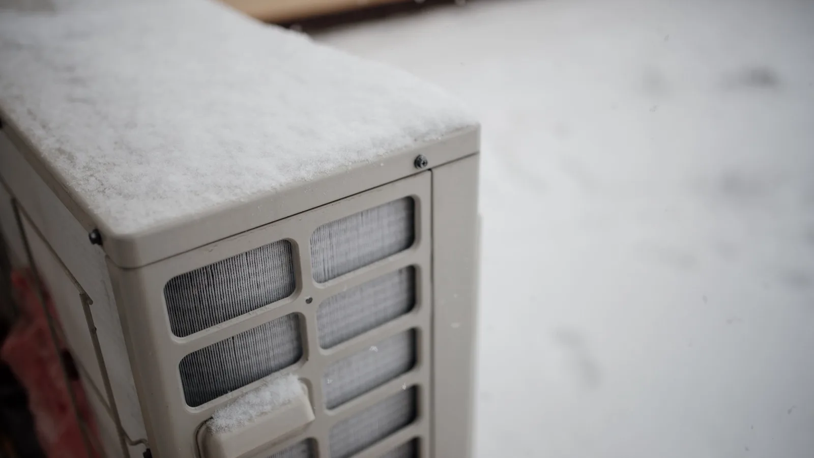 Best cold climate DIY mini split — a ductless mini split outdoor condenser covered in fresh snow during a winter snowfall, the low ambient heating conditions MRCOOL DIY 5th Gen Hyper Heat and Zone Air are rated for