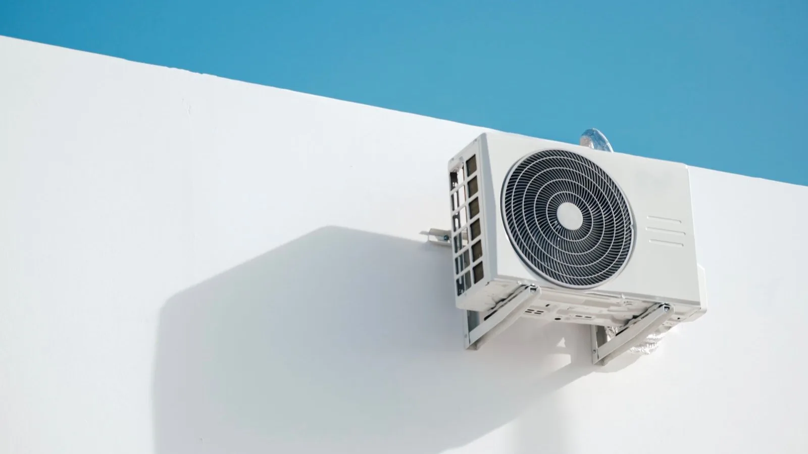 Mini split no vacuum pump install — the outdoor condenser of a pre-charged line set DIY mini split mounted on a wall bracket, with the sealed, insulated line set running into the wall, no vacuum pump or manifold gauges attached